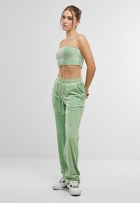 Zeleni baršunasti crop top s detaljem logotipa u paru s odgovarajućim velur joggericama. Outfit sadrži prilagođeni kroj i pojas s vezicom. Bijele tenisice.