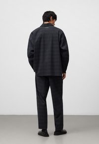 Donkergrijze, geruite blouse met een puntkraag en lange mouwen, gecombineerd met een bijpassende, taps toelopende broek. Soepele textuur en een relaxte pasvorm.