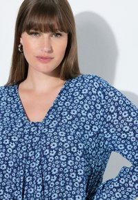 Granatowy top w kwiaty z jasnoniebieskimi stokrotkami, z dekoltem w kształcie litery V i detalem plisowania, wykonany z lekkiego materiału.