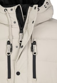 Beige insulated jacket featuring a zip closure, adjustable drawstrings, black accents, and snap buttons; smooth texture and hooded design.