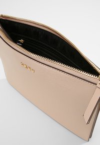 Beige synthetic leather clutch with gold-tone hardware. Features a zip closure, interior pockets, and a textured surface.