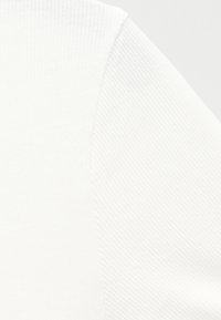 Κοντινό σε λευκό ύφασμα που δείχνει κυψελωτή υφή και ραπές κατά μήκος μιας ραφής, αναδεικνύοντας λεπτομέρειες του υλικού του ρούχου.