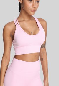 Różowy sportowy crop top z dekoltem w serek, potrójnymi ramiączkami z jednej strony oraz gładkim, elastycznym materiałem. Żebrowany pas na dole.