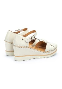 Sandales compensées en cuir blanc avec un design à lanières, boucle réglable et détails cousus sur le coin et la semelle. Doublure intérieure texturée.