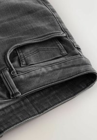 Jeansi din denim gri cu o suprafață texturată, având o singură buzunar cu elemente de metal și cusături contrastante de-a lungul cusăturilor.