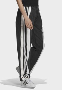 Svarta denimbyxor med vita sidopaneler som har tre svarta ränder och tryckknappar ner längs sidan, stylad med vita sneakers.