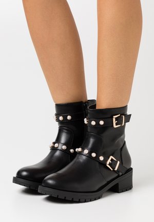 Botas de tobillo de cuero negro con adornos de perlas decorativas y hebillas, con una suela texturizada para agarre. Acabado liso y punta redondeada.