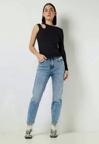 Črn dolg rokav s asimetričnim krojem in modre kavbojke. Kavbojke imajo oprijet kroj in svetlo pranje s subtilnim zamegljenjem.