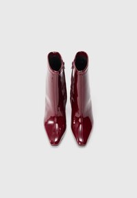Botas de tornozelo em pele envernizada burgundy com um acabamento brilhante, bico apontado e fecho de correr na parte de trás, apresentando um design elegante e aerodinâmico.