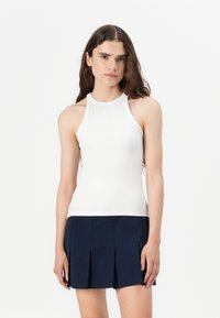 Weißes, geripptes Halterneck-Top mit körperbetonter Passform und geradem Saum, kombiniert mit einem marineblauen, gefalteten Miniskirt aus einem glatten Stoff.