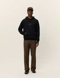 Felpa nera con cappuccio e tasca frontale, logo bianco piccolo; abbinata a pantaloni a quadri marroni e scarpe nere. Il cappello ha un motivo a scacchi.