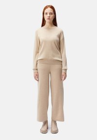 Beige stickad tröja med rund halsringning, i kombination med matchande vida byxor, allt tillverkat av mjukt material, kompletterat med beige kraftiga stövlar.