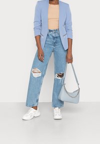 Světle modrý blazer přes béžový žebrovaný top, doplněný o roztrhané široké džíny a bílé tenisky. Drží světle modrou kabelku s řetízkovým detailem.