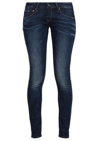 Vaqueros de denim azul oscuro, de corte ajustado. Con detalles deshilachados cerca de las rodillas, arrugas sutiles y diseño clásico de cinco bolsillos.