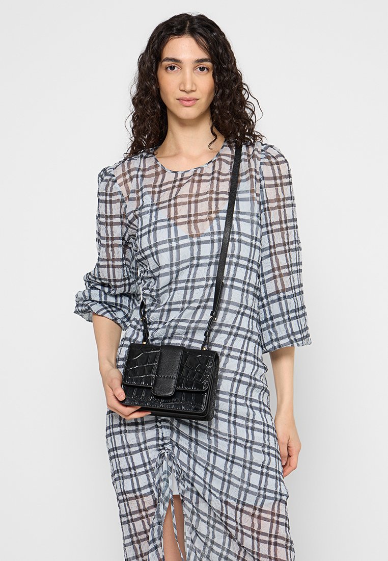 Czarna torebka crossbody z sztucznej skóry o teksturowanym wzorze krokodyla, w kształcie prostokąta, z klapą, noszona przez modelkę.