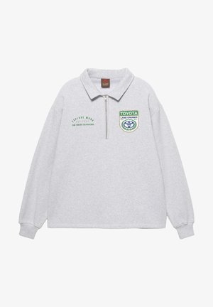 Grauer, langärmeliger Pullover mit einem Reißverschluss am Kragen. Mit grünen und blauen gestickten Logos und Texten. Der Text enthält die Schriftzüge "EXPLORE MORE" und "TOYOTA LAND CRUISER".