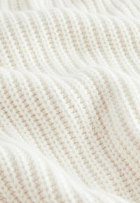 Gros plan sur un tissu tricoté doux, blanc cassé, avec un motif texturé de petits points en relief formant des lignes horizontales.