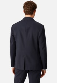 Giacca blu navy con uno spacco singolo, texture liscia e polsini abbottonati, progettata per una vestibilità su misura, vista da dietro.