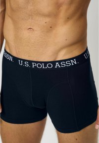 Fekete pamut boxeralsó, testhezálló szabással, fehér logós derékpánttal, amelyen a "U.S. POLO ASSN." felirat olvasható. Simább textúrájú, minta nélkül.