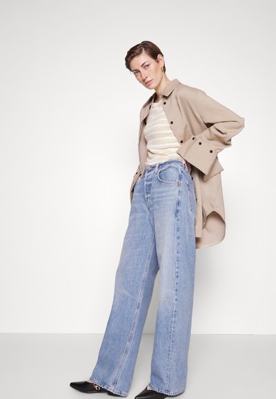 Veste chemise beige oversize, chemise crème rayée, et jean en denim large bleu clair. Escarpins noirs à bout pointu, textures de tissu lisses.