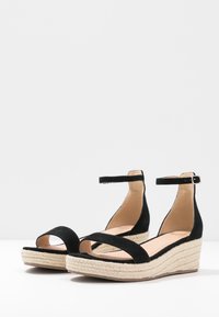 Black suede wedge sandals with a jute-wrapped platform, featuring a single strap across the toes and an adjustable ankle strap.