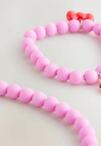 Närbild av ett rosa pärlhalsband, som har runda matta pärlor och en röd detalj som liknar en rosett, mot en mjuk neutral bakgrund.