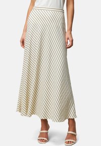 Crèmekleurige rok met diagonale zwarte strepen, uitlopende vorm, gestructureerde stof en een brede tailleband. Draagt met witte sandalen.