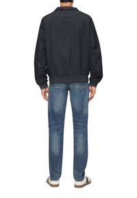 Donker marineblauwe bomberjack met een geribde kraag en manchetten, gecombineerd met medium-wash jeans en witte sneakers, gezien vanaf de achterkant.