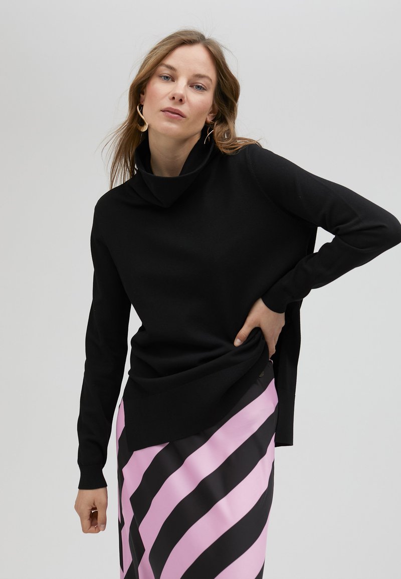 Svart cowl-neck tröja med långa ärmar, som har en avslappnad passform. Kombinerad med en randig kjol i rosa och svart för kontrast.