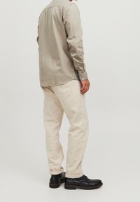 Lichtgrijze longsleeve shirt met knopen, gecombineerd met crèmekleurige spijkerbroek en zwarte leren schoenen, gezien van achteren.