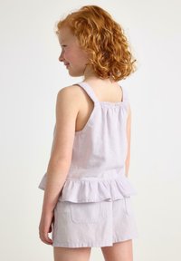 Lilac peplum-toppi, jossa on röyhelöhelma, ohuet olkaimet ja laskostettu takaosa, yhdistettynä samanvärisiin lilac-shortsihin, joissa on kaksi etutaskua.