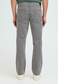 Sive jeans hlače s ravnim krojem, ki vsebujejo klasičen pet-pocket dizajn in subtilno teksturo. Zadnji pogled prikazuje dva zadnja žepa.
