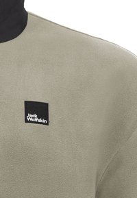 Fleece pullover in light olive green, featuring a high neck and textured surface. Black square logo patch stitched on the front.