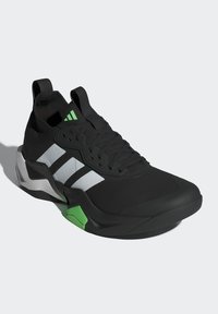Chaussure de sport noire avec une tige texturée, ornée de trois rayures blanches, d'un accent vert et d'une semelle épaisse.