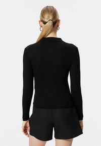 Schwarzes, geripptes Langarmoberteil mit einer figurbetonten Passform und einem klassischen Kragen, kombiniert mit schwarzen Shorts. Die Textur wirkt weich und dehnbar.