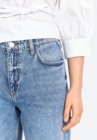 Jeans in denim azzurro chiaro con vita alta, design classico a cinque tasche e cuciture arancioni a contrasto. Texture liscia con leggeri sbiancamenti.