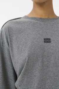 Sweatshirt en coton gris avec un col rond, des détails subtils aux épaules et un logo brodé sur la poitrine. Texture lisse.