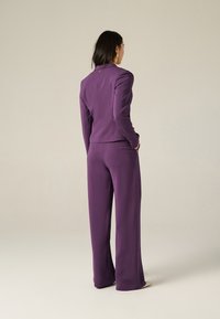 Costume ajusté violet comprenant un blazer cintré avec un revers en notch et un pantalon à jambes larges. Texture lisse avec des lignes épurées et un minimum de détails.