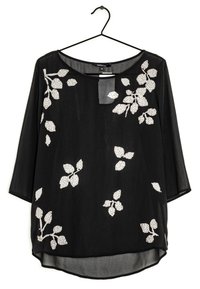 Schwarze Bluse mit 3/4-Ärmeln, die ein florales Muster in Weiß mit Blättern und Akzenten aufweist. Hergestellt aus leichtem, transparenter Stoff, mit rundem Ausschnitt.