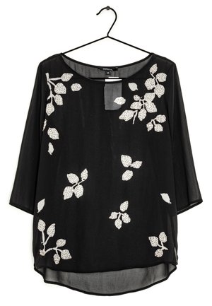 Schwarze Bluse mit 3/4-Ärmeln, die ein florales Muster in Weiß mit Blättern und Akzenten aufweist. Hergestellt aus leichtem, transparenter Stoff, mit rundem Ausschnitt.