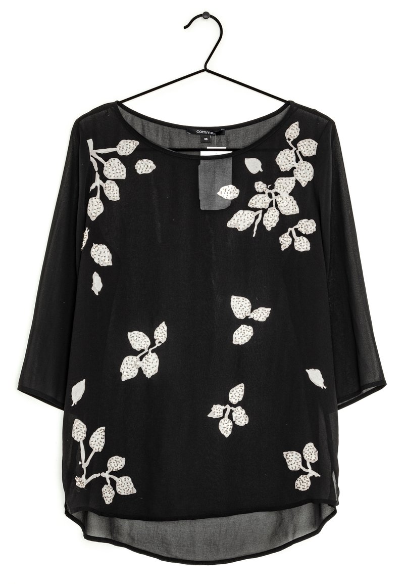 Blouse noire à manches 3/4, ornée d'un motif floral blanc avec des feuilles et des accents. Fabriquée en tissu léger et transparent, avec un décolleté arrondi.