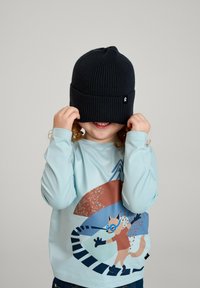 Czarna dzianinowa czapka, ribbowany wzór, zasłania oczy. Jasnoniebieska koszula z długim rękawem z kolorową grafiką zwierząt. Ręce dziecka trzymają czapkę.