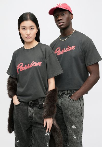 Γκρι βαμβακερά T-shirt με τη λέξη "Passion" γραμμένη με κόκκινα γράμματα. Μαύρα τζιν τζιν με σχέδια κουνελιού. Το μοντέλο φοράει μανίκι από γούνα και κόκκινο καπέλο.