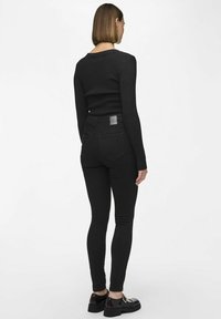 Svart ribbet langermet topp kombinert med svarte skinny jeans. Jeansene har baklommer og en firkantet lærlapp på livlinjen.