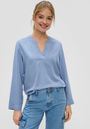 Chemise à manches longues bleu clair avec un col en V, présentant une texture lisse et une coupe décontractée, associée à un pantalon en denim bleu clair.