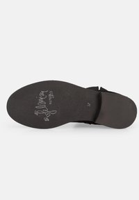 Suela de zapato de ante negro con un diseño plano. Presenta una textura natural y detalles de marca grabados. Tamaño '37' estampado visible.