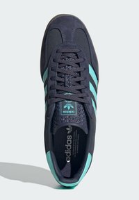 Scarpa sportiva in suede blu scuro con tre strisce turchesi e dettagli, linguetta testurizzata e soletta ammortizzata visibile dalla vista superiore.