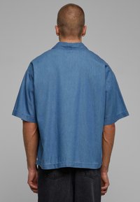 Modra denim kratka srajca s sproščenim krojem, ki ima preprost ovratnik in čista zaključka. Gladka tekstura, brez vzorcev ali okrasnih elementov.