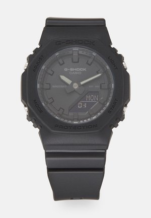 Svart G-Shock klokke med digital skjerm, teksturert bezel og reim i resin. Funksjoner inkluderer flere klokker, beskyttende kapsling og knapper.