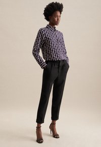 Camicia a maniche lunghe a pois viola con colletto, abbinata a pantaloni neri a vita alta e tacchi neri con cinturini. Texture lisce.